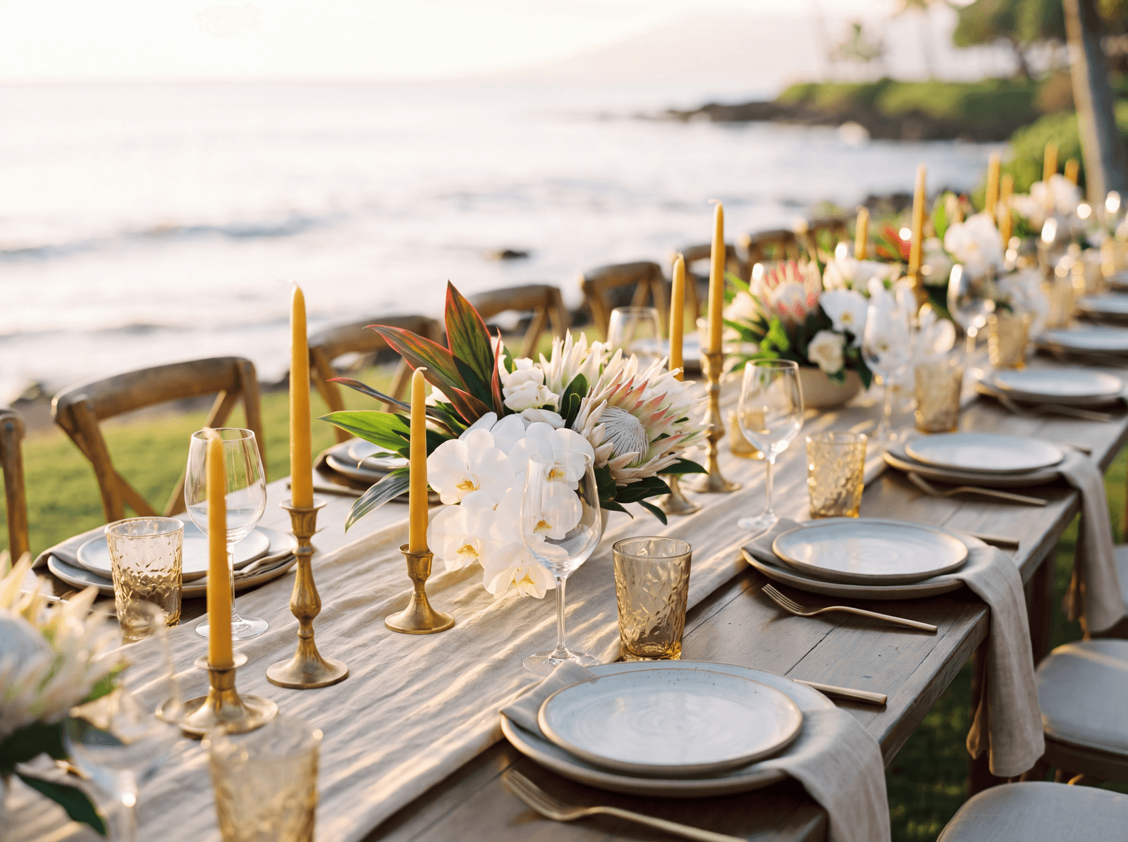 Oceanfront dinner table set with orchids and ti leaves at golden hour