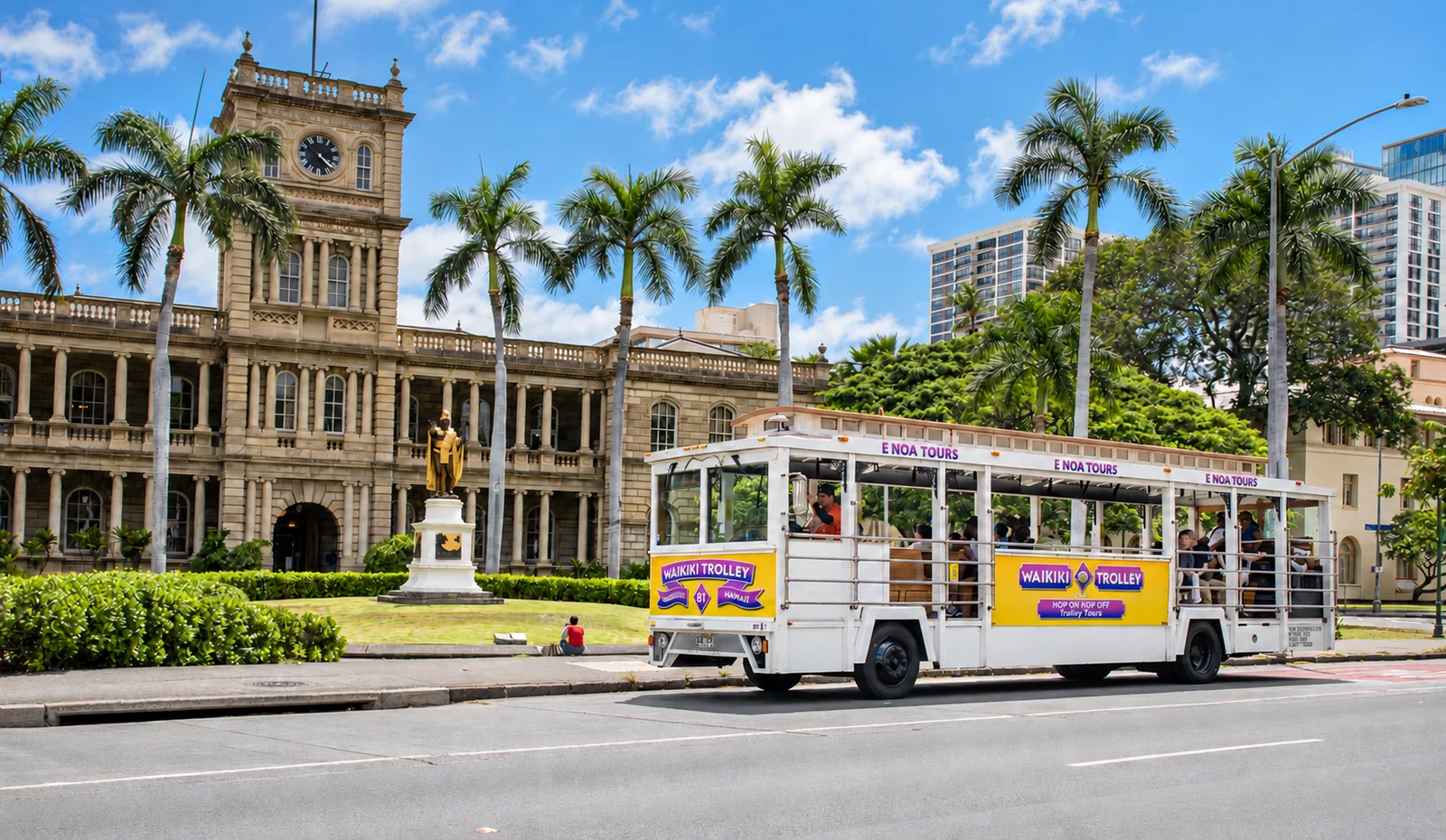 Sightseeing trolley beside a historic Honolulu building and statue