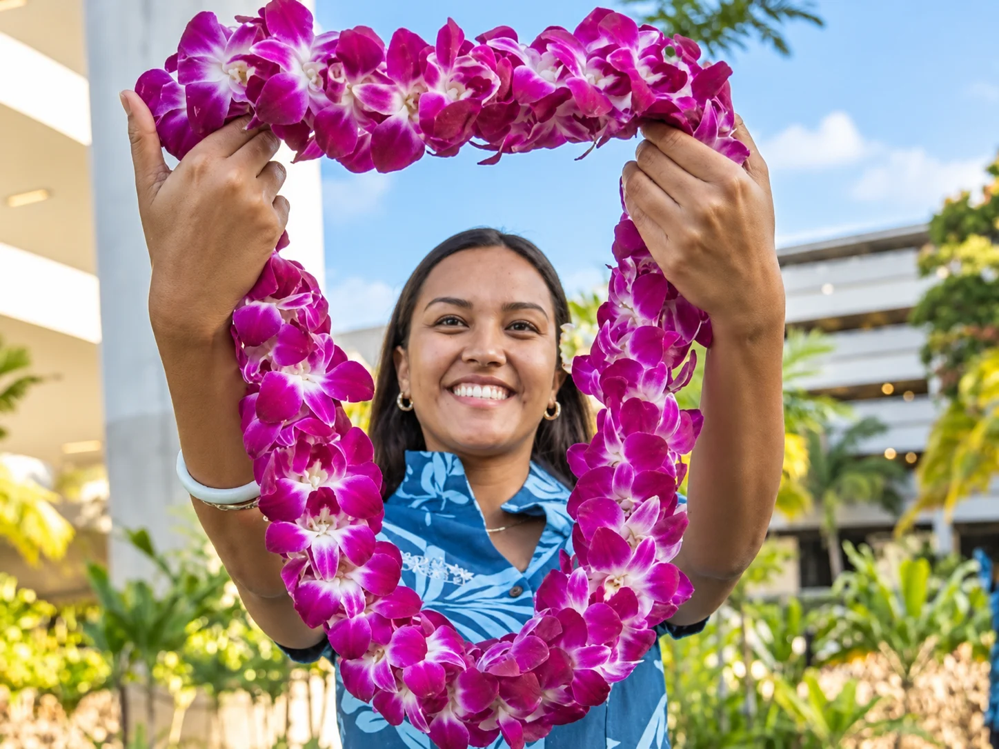 Smiling host holding a purple orchid lei in welcome