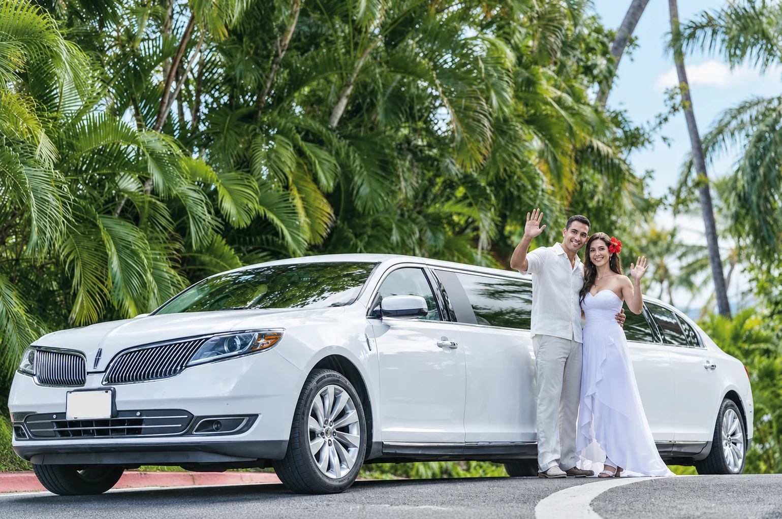 Wedding couple smiling and waving beside a white limousine