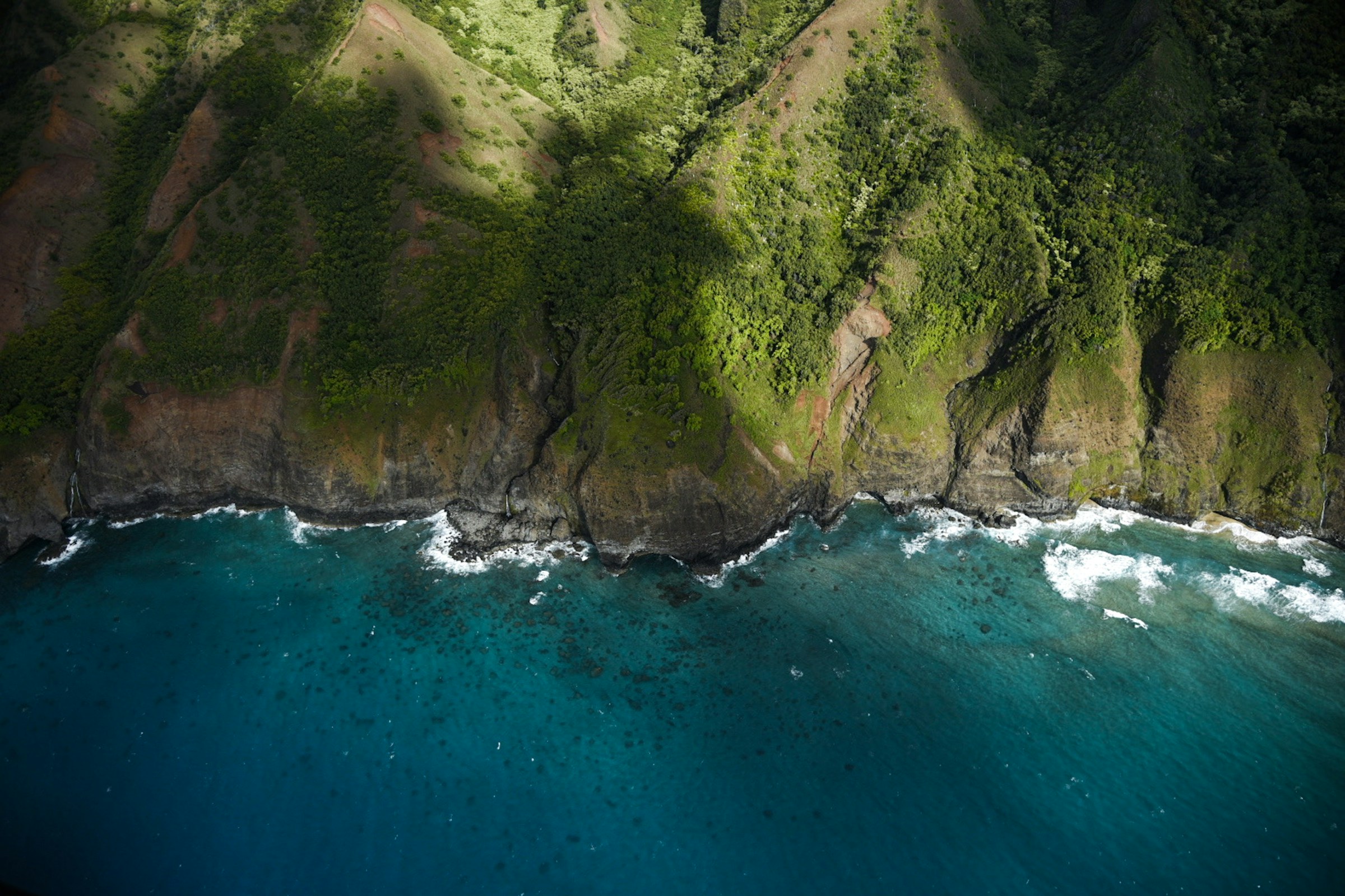 Green cliffs of Kauaʻi’s Nā Pali Coast meeting the turquoise Pacific Ocean